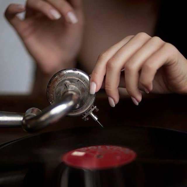 Main de femme posant une aiguille sur un vinyle rétro — toucher, précision, soin